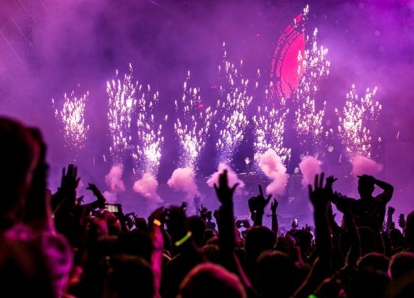 A cheering crowd in front of purple sparks flying on stage.